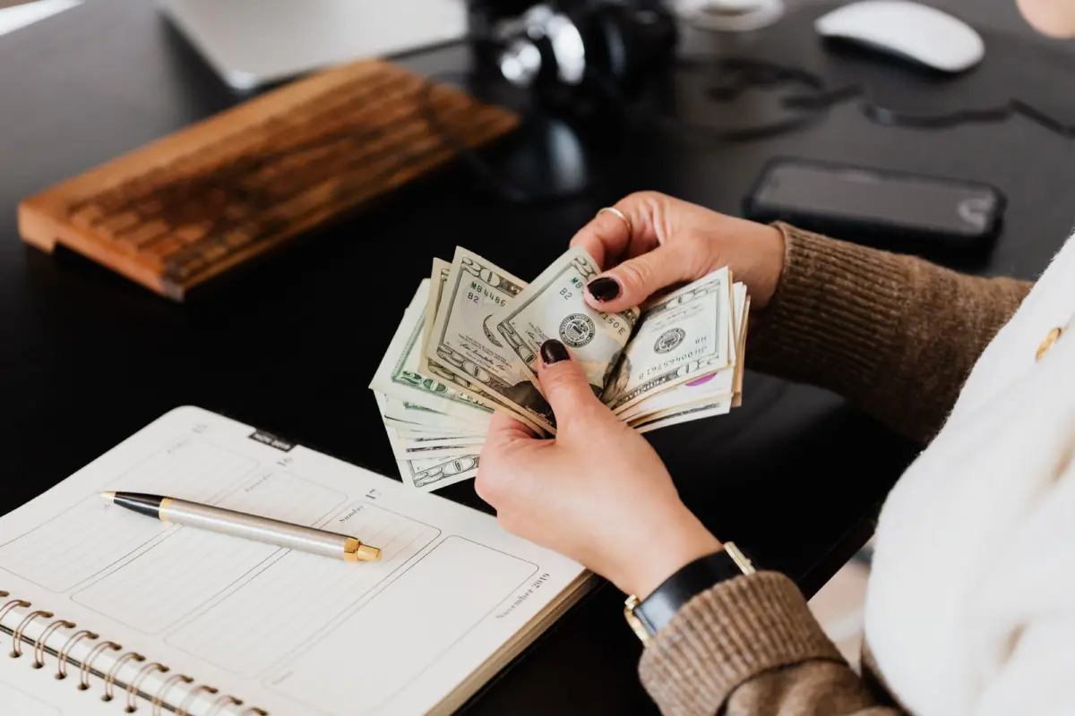 A woman counting cash next to a planner